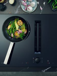 Тиган със зеленчуци върху вентилиран плот за готвене в наситено черно 