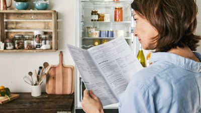 Eine Frau liest eine Gebrauchsanleitung, während im Hintergrund ein geöffnetes Kühl-Gefriergerät zu sehen ist.