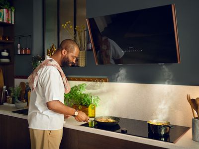 Man with towel over shoulder frying, steam extracted by inclined hood 