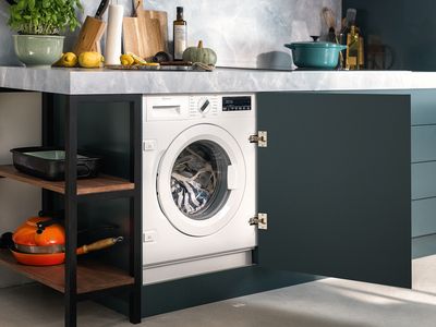 A washing machine inside an open kitchen cupboard beneath the countertop