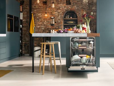 An industrial kitchen with an open dishwasher integrated in a kitchen island at the centre