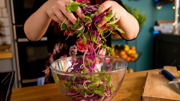 Person mixing salad with hands in bowl