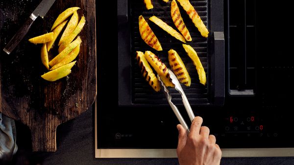 Person grilling mango slices