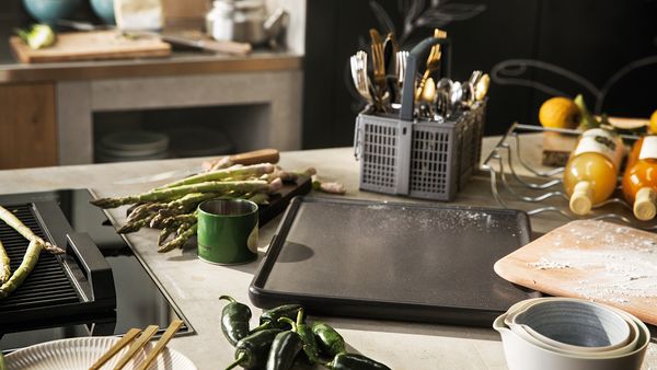 Différents accessoires NEFF, asperges, épices, poivrons et boissons sur un comptoir de cuisine de couleur claire.