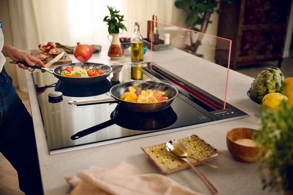 Der herausfahrbare Dunstabzug aus Glas mit verschiedenen Gerichten auf dem Kochfeld 