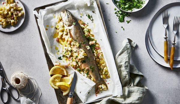 A baked arctic char with diced kiwis, apples and charlottes along with lemon slices in a oven dish.