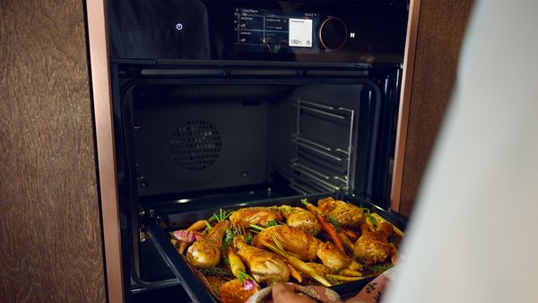 Tray full of roast chicken being placed into an oven with Brushed Bronze side strips 
