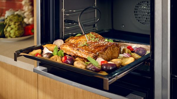 Roast beef and vegetables on oven tray with meat thermometer  