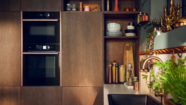 Image of microwave stacked above oven, with Seamless Combination in Brushed Bronze, dark brown wood kitchen 