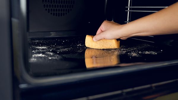 A videó bemutatja a pirolitikus tisztítást, egy kéz szivaccsal takarítja a sütőt 