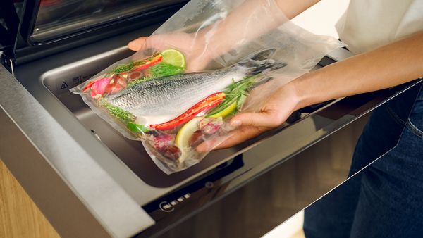 A closer view inside a Sous-vide Drawer beneath an oven into which a person is placing a sous-vide bag with prepared food