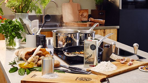 A selection of additional cooking utensils and care products assembled on a kitchen island in front of a hob in use