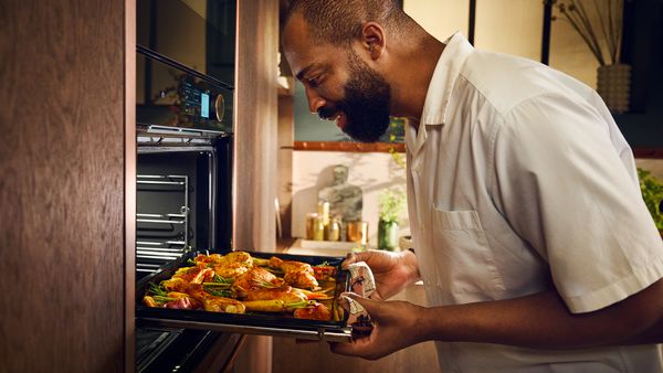 Egy férfi egy rejtett ajtós beépített sütő közelében áll, miközben kihúzza az ételt tartalmazó sütőtálcát