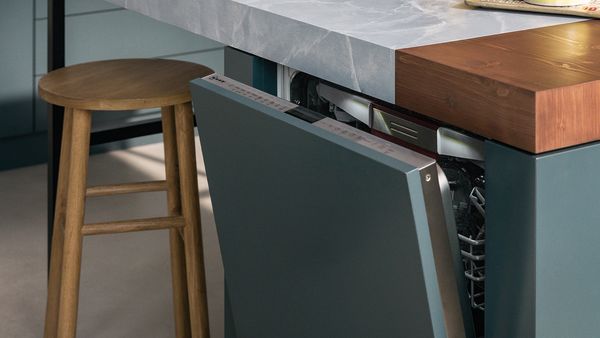 Közelkép egy teljesen beépített mosogatógépről, enyhén nyitott ajtóval, amelynek színe megegyezik a konyháéval