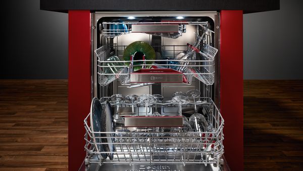 A free-standing, open and illuminated dishwasher with three baskets partially filled