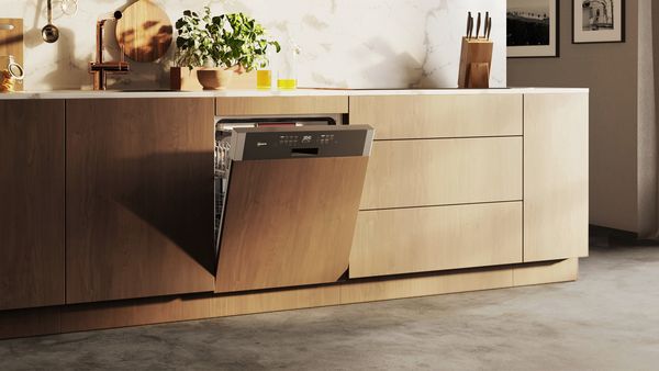 A light-wood kitchen unit with a slightly open semi-integrated dishwasher with a visible control panel