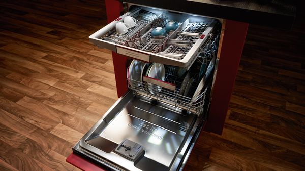 A free-standing, open dishwasher with an illuminated cutlery drawer pulled out at the top
