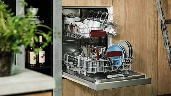 A 60 cm dishwasher with an open door incorporated at a comfortable height in a light-brown kitchen cabinet