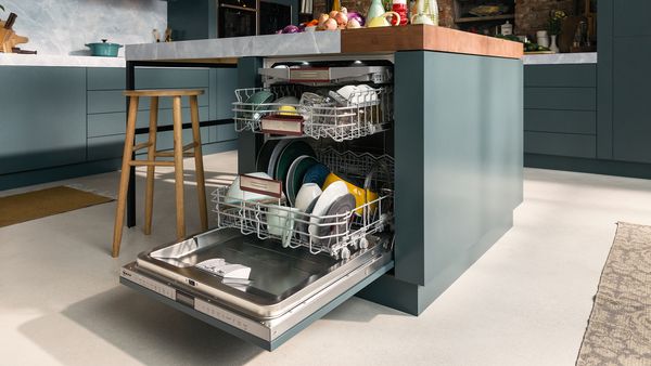 A fully-integrated 60 cm dishwasher with an open door to show three filled baskets