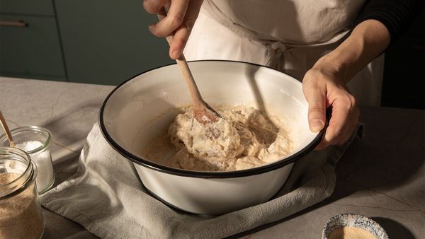 a bowl with a dough which someone mixes with a wooden spoon