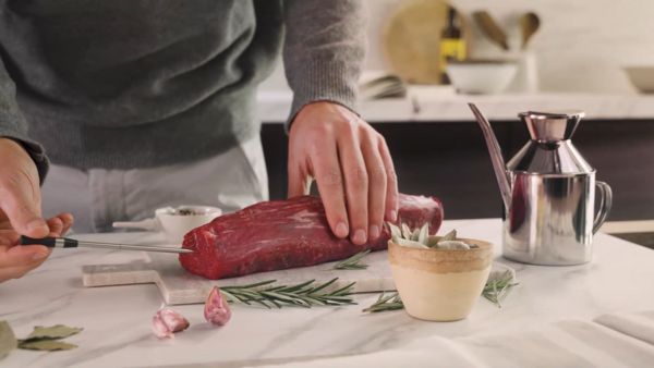 A person in a grey sweater prepares a raw cut of meat on a marble countertop by inserting NEFF meatprobe.