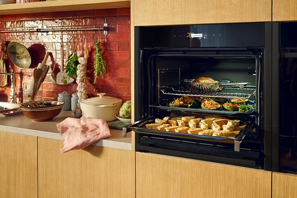 NEFF oven with meat probe inserted in tray of roast meat and vegetables.