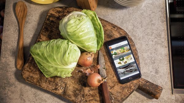 Mobile phone and food on chopping board to show Home Connect app whilst cooking