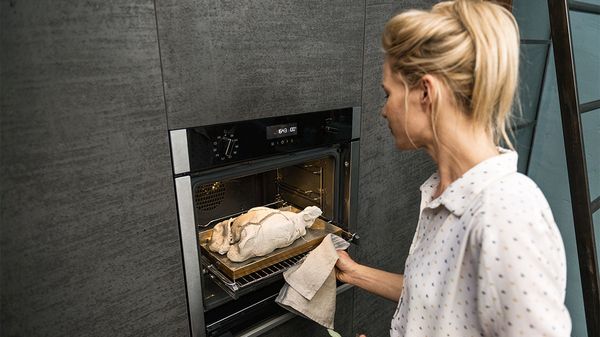 Woman removing chicken from NEFF Slide&Hide oven