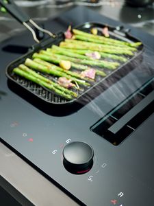 Vented cooktop close-up in Deep Black with green vegetables in griddle pan 