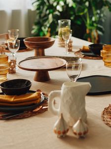 Stalo vaizdas su linine staltiese, vyno taurėmis, moliniais padėklais tortams bei oranžinėmis stiklinėmis vazomis 