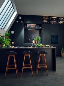 Et kjøkken med mørke overflater og høy kjøkkenøy. To innebygde ovner i høyskap bak i bildet