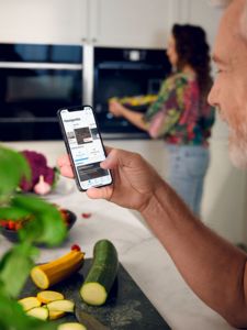 Man in kitchen scrolling through neff homeconnect app