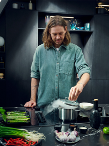  A man stands in a modern kitchen, preparing food with various utensils and ingredients on the counter. 