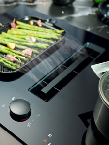 A stove top featuring a grill and a pot of food, equipped with a venting hob for efficient cooking. 