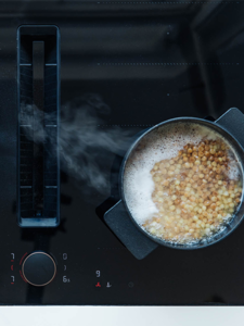 A pot of beans simmering on a stove top, steam rising, showcasing a home-cooked meal in progress.