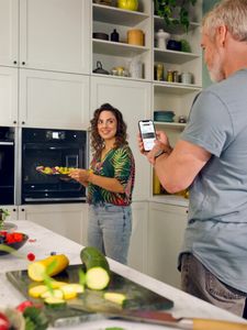 A man and woman standing together in a modern kitchen, engaged in conversation while preparing a meal.  