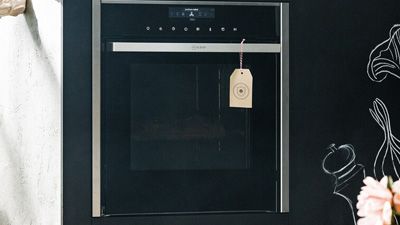 Beige label with red and white string hangs on a black NEFF built-in oven.