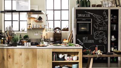 A kitchen with a wooden and stone worktop and a lot of clamps, ladder and lots of light