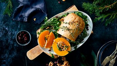 A sliced pumpkin, stuffed with cheddar, kale and walnut risotto, garnished with green herbs