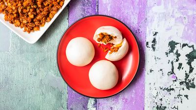 Three steamed buns filled with Kimchi pork on a red plate