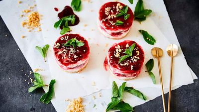 Three frozen raspberry cream desserts, garnished with mint leaves and cookies crumble
