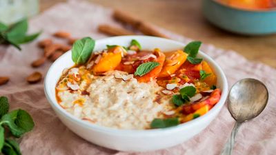 A white bowl with cinnamon porridge, topped with caramelized oranges and mint leaves