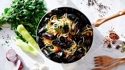 Spaghetti with mussels in their shells garnished with parsley in a frying pan