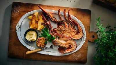 A cooked lobster cut open in the middle with fries, a grilled piece of lemon and some dip