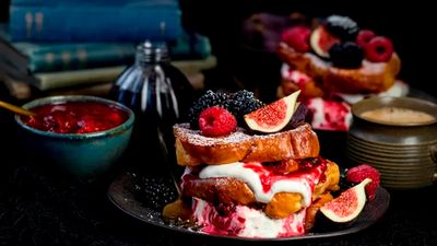Three pieces of french toast and between all of them, there is creme fraiche and a spoon of blackberry compote