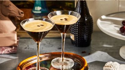 A stylish martini with a foamy coffee topping, beside grapes and decorative objects, creating a chic ambiance.