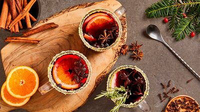 Cups of mulled wine with spices and oranges on a wooden board.