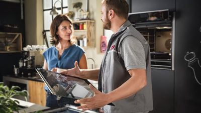 Tecnico che tiene lo sportello esterno di un forno sotto lo sguardo del cliente che sorride.