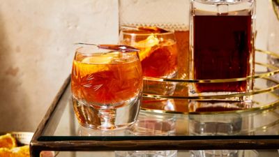 Two whiskey glasses with orange slices sit on a reflective table next to a bottle of liquor, creating an inviting bar scene.