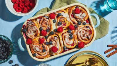 Baked cinnamon rolls with fresh berries and a white frosting in a rectangular baking dish on decorated table